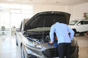 bonito africano homem de negocios é examinando uma carro antes comprando isto, ele Verificações todos características e características do auto foto