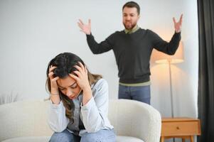 emocional homem gesticulando e gritando às dele esposa, jovem casal tendo brigar às lar. doméstico Abuso conceito foto