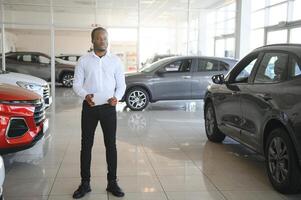 retrato do bonito africano americano vendedor às local de trabalho dentro carro sala de exposições foto