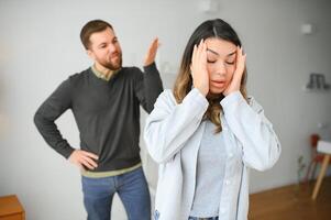 emocional homem gesticulando e gritando às dele esposa, jovem casal tendo brigar às lar. doméstico Abuso conceito foto