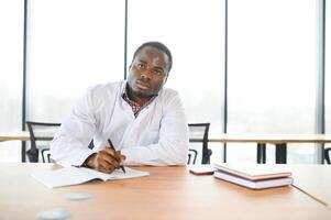 africano médico sentado cansado às a mesa dentro a hospital foto