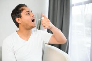 indiano homem doente às lar, frio, gripe. uma homem usa uma garganta spray foto