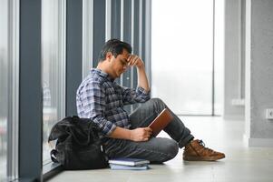 cheio comprimento do depressivo Garoto sentado com mochila dentro escola corredor foto