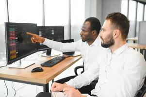 dois homens colegas comerciantes sentado às escrivaninha às escritório monitoramento estoque mercado foto