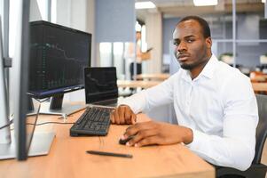 africano americano comerciante trabalho às computador com exibido tempo real ações foto