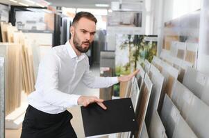 retrato do uma cerâmico telha vendedor. a vendedor carrinhos contra a fundo do uma ampla sortimento do azulejos foto