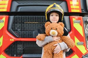 uma Garoto vestindo uma bombeiro capacete perto uma fogo caminhão. foto