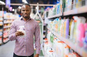 africano homem segurando garrafa do família produtos químicos dentro grande loja foto