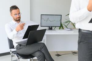 milenar escritório empregado dentro óculos sentado às escrivaninha dentro frente do computador portátil sorridente olhando às Câmera. bem sucedido trabalhador, carreira avançar e oportunidade, proprietário do próspero o negócio conceito. foto