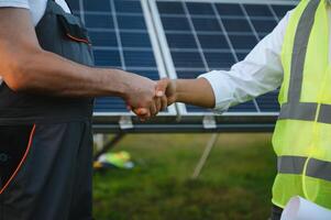 trabalhadores tremendo mãos em uma fundo do solar painéis em solar poder plantar foto