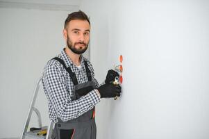 eletricista dentro uniforme montagem elétrico tomadas em a branco parede dentro de casa foto