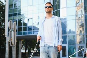 jovem bonito cego homem caminhando com bastão dentro Cidade foto