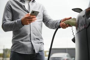 homem segurando poder cobrando cabo para elétrico carro dentro ao ar livre carro parque foto