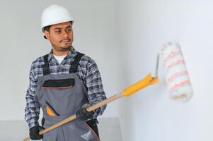 a indiano apartamento reparar trabalhador tintas uma branco parede com uma rolo. foto