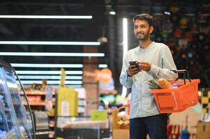 indiano homem usando Smartphone às mercearia fazer compras. foto