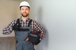 retrato do uma confiante reparador com barba em pé dentro esvaziar apartamento foto