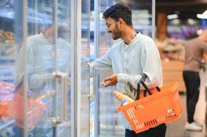 retrato do feliz indiano homem em pé dentro frente do a produtos contador dentro uma mercearia loja. homem comprando mercearia para casa dentro supermercado. foto