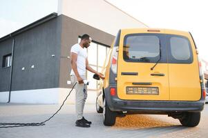 africano americano homem carrinhos Próximo para elétrico Entrega vans às elétrico veículo cobrando estação foto