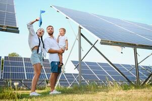 jovem família do três é agachado perto fotovoltaico solar painel, pequeno Garoto e pais. moderno família conceito. a conceito do verde energia foto