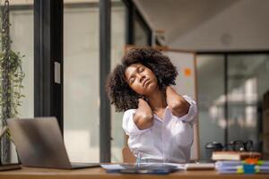 Preto mulher obtendo fisicamente ativo a partir de fadiga sentado às uma escrivaninha. cansado a partir de trabalhar, torção vencimento para dor, escritório síndrome do escritório trabalhadores foto