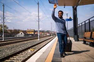 feliz homem com mala de viagem em pé e acenando em uma estrada de ferro estação. foto