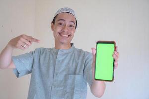 muçulmano ásia homem feliz, sorridente quando mostrar a Smartphone com verde tela quando Ramadã celebração. a foto é adequado para usar para Ramadhan poster e muçulmano conteúdo meios de comunicação.