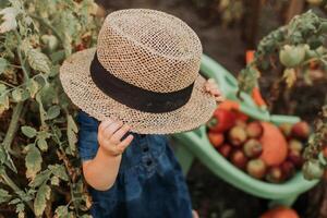 retrato do uma fofa pequeno menina dentro uma azul vestir e uma Palha chapéu dentro a outono jardim. jovem agricultor foto
