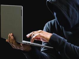 mão hacker espião homem 1 pessoa dentro Preto moletom com capuz sentado em mesa olhando computador computador portátil usava Conecte-se senha ataque segurança para dados digital Internet rede sistema noite Sombrio fundo cópia de espaço foto