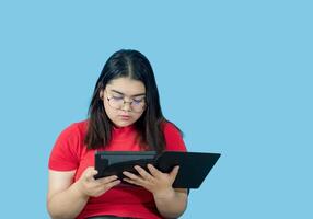 retrato o negócio menina jovem mulher ásia gordo gordo fofa lindo bonita 1 pessoa vestindo vermelho camisa dentro escritório segurando digital tábua e sorridente em pé com cópia de espaço em isolado azul terra negra foto