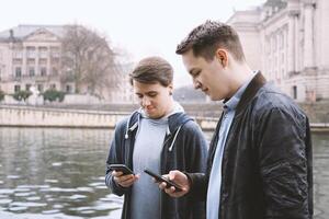 dois Móvel telefone viciado masculino adolescentes em pé juntos olhando às Smartphone foto