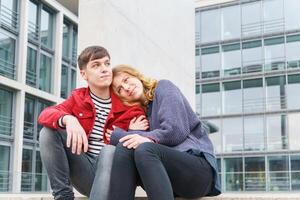 jovem casal sentado em passos dentro frente do moderno construção foto