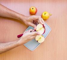 fechar acima masculino mãos cortar a maçã para dentro fatias. topo Visão do preparando frutas sobre cozinha mesa. foto