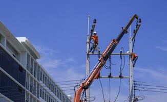 dois eletricistas com guindaste caminhão estão trabalhando para instalar elétrico transmissão em poder postes com construção contra azul céu fundo foto