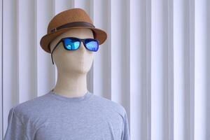 fechar acima do masculino manequim dentro cinzento camiseta com oculos de sol e fedora chapéu em branco de madeira parede fundo foto