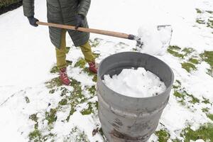 meia idade mulher é colecionar neve dentro uma barril com uma pá, natural Recursos foto