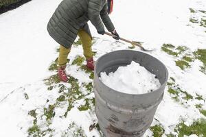 meia idade mulher é colecionar neve dentro uma barril com uma pá, natural Recursos foto