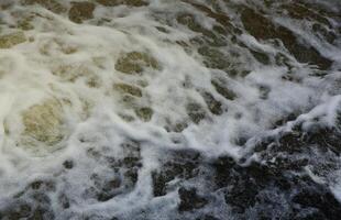 ondas de água do rio e do mar se encontram durante a maré alta e maré baixa. superfície da água do mar tempestuoso azul profundo com espuma branca e padrão de ondas, foto de fundo