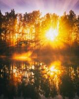 alvorecer em uma lago ou rio com uma céu refletido dentro a água, bétula árvores em a costa e a raios solares quebra através eles e névoa dentro outono. estética do vintage filme. foto