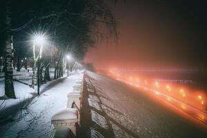 inverno parque às noite com lanternas, Visão para estrada com carro movimento, calçada e árvores dentro nebuloso clima. vintage filme estética. foto