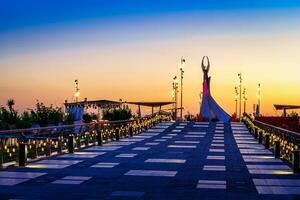 uzbequistão, Tashkent - abril 25, 2023 a território do a parque Novo uzbequistão com monumento do independência dentro a Formato do uma estela com uma humo pássaro às crepúsculo. Visão a partir de uma ponte. foto