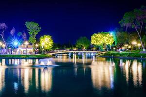 borrado água fluxos do uma fonte dentro a artificial lago dentro uma noite parque com lanternas, uma ponte e árvores foto