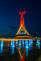 uzbequistão, Tashkent - pode 5, 2023 iluminado monumento do independência dentro a Formato do uma estela com uma humo pássaro, fontes e acenando bandeiras dentro a Novo uzbequistão parque às período noturno. foto