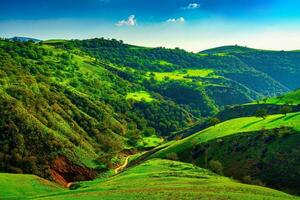 colinas e montanhas coberto com jovem verde Relva e iluminado de a Sol em uma ensolarado dia. foto