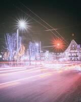 noite inverno cidade com Natal ou Novo ano decorações, abeto e vestígios do faróis do comovente carros. vintage filme estética. foto