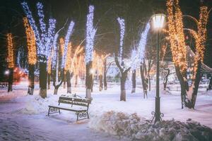 inverno parque às noite com Natal decorações, brilhando lanternas, calçada coberto com neve e árvores vintage filme estética. foto