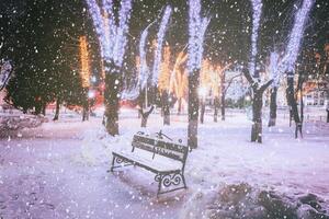 queda de neve dentro uma inverno parque às noite com decorações, brilhando lanternas, calçada coberto com neve e árvores vintage filme estética. foto
