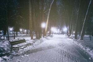 inverno noite parque com árvores, brilhando lanternas e bancos coberto com neve. vintage filme estética. foto