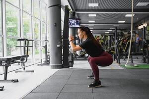 lado Visão retrato do uma jovem mulher fazendo agachamentos às ginástica academia. foto