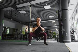 lado Visão retrato do uma jovem mulher fazendo agachamentos às ginástica academia. foto