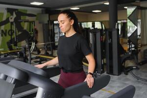 atraente jovem Esportes mulher é trabalhando Fora dentro academia. fazendo cardio Treinamento em esteira. corrida em esteira foto